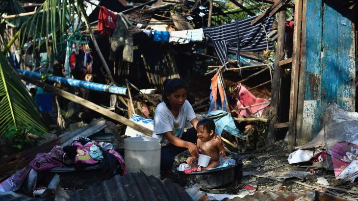 Mulher dá banho em seu filho em meio à destruição causada pelo tufão Rai em Carcar, nas Filipinas (VICTOR KINTANAR / AFP)