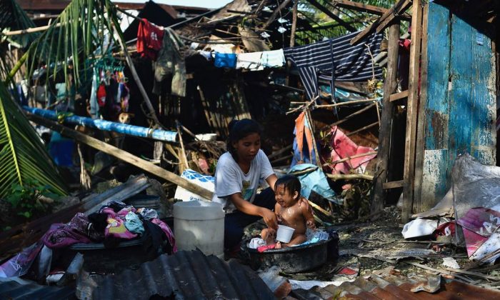 Mulher dá banho em seu filho em meio à destruição causada pelo tufão Rai em Carcar, nas Filipinas (VICTOR KINTANAR / AFP)