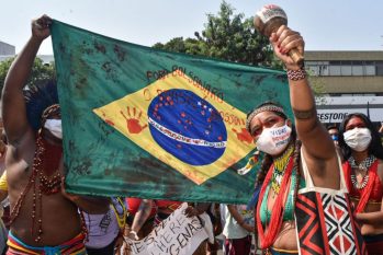 Indígenas seguram Bandeira do Brasil manchada de vermelho, imitando sangue, com frase 