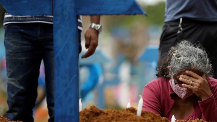 Idosa chora ao lamentar morte de ente em frente a túmulo em cemitério de Manaus. (Reuters)