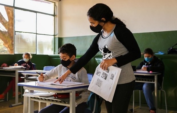 Professora ajuda aluno em sala de aula (Reprodução/ Internet)