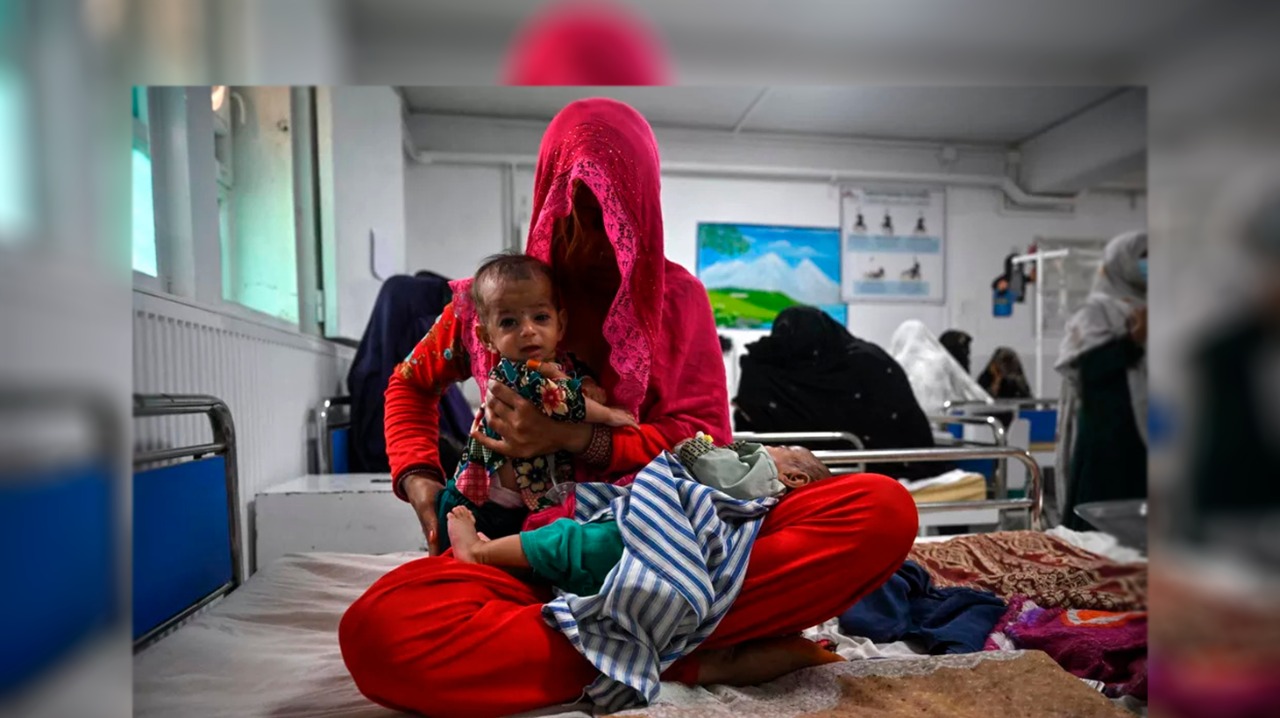 Uma mãe senta em uma cama de hospital com os gêmeos de quatro meses, na ala de atendimento à desnutrição, em Lashkar Gah, no Afeganistão (Lillian Suwanrumpha/AFP)