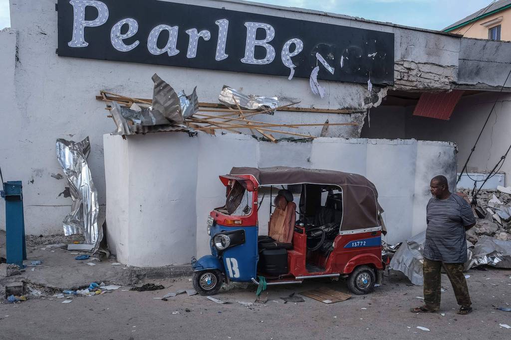 Homem caminha em frente a hotel, em Mogadíscio, destruído após a invasão de extremistas (Hassan Ali Elmi/AFP)