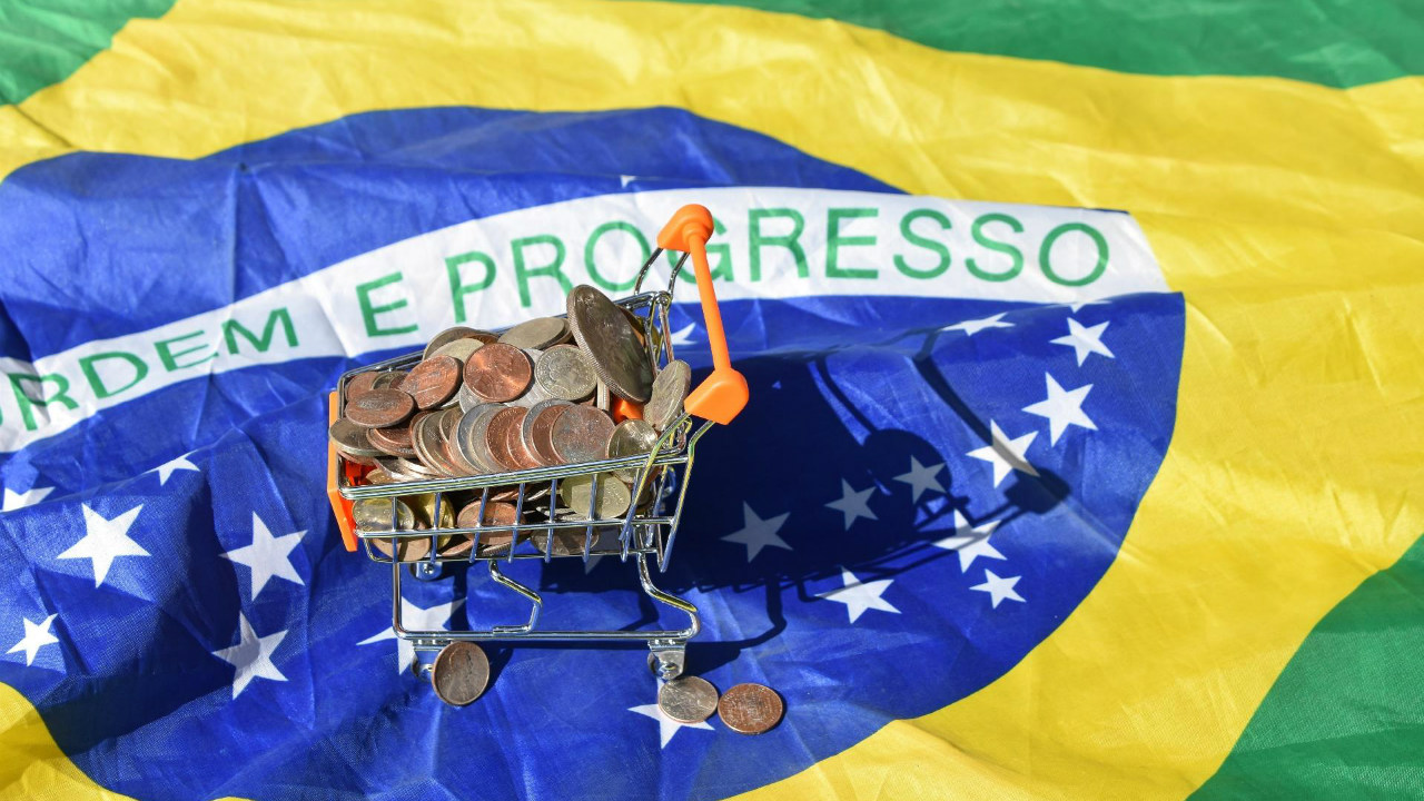 A bandeira brasileira e um carrinho de compras com moedas dentro (Reprodução/Mercado e Consumo)