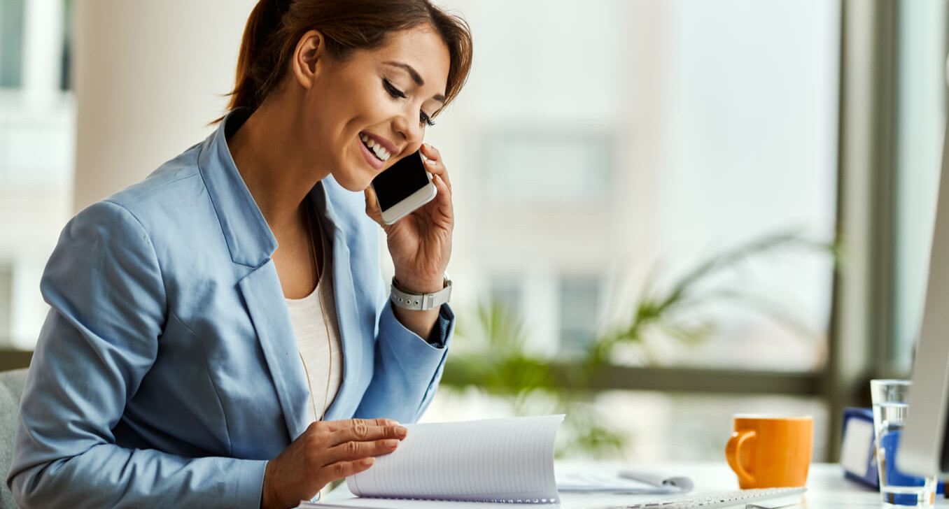 Mulher fala ao celular enquanto folheia uma agenda (Reprodução)