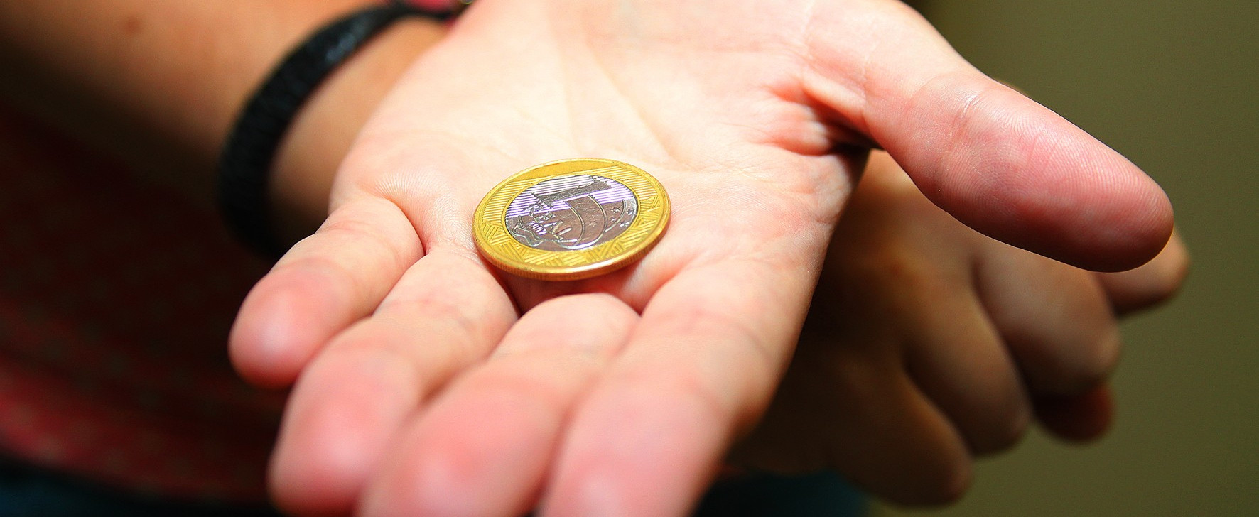 Detalhe de mão segurando moeda de R$ 1 (um real). (Marcos Santos/USP Imagens)